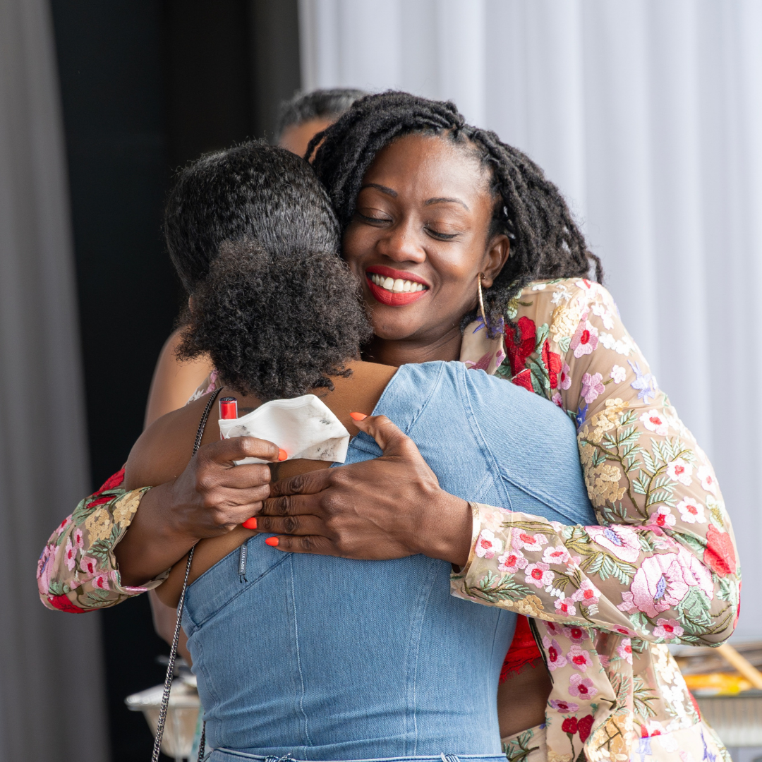 Two women embracing and laughing at a HerPlum community gathering